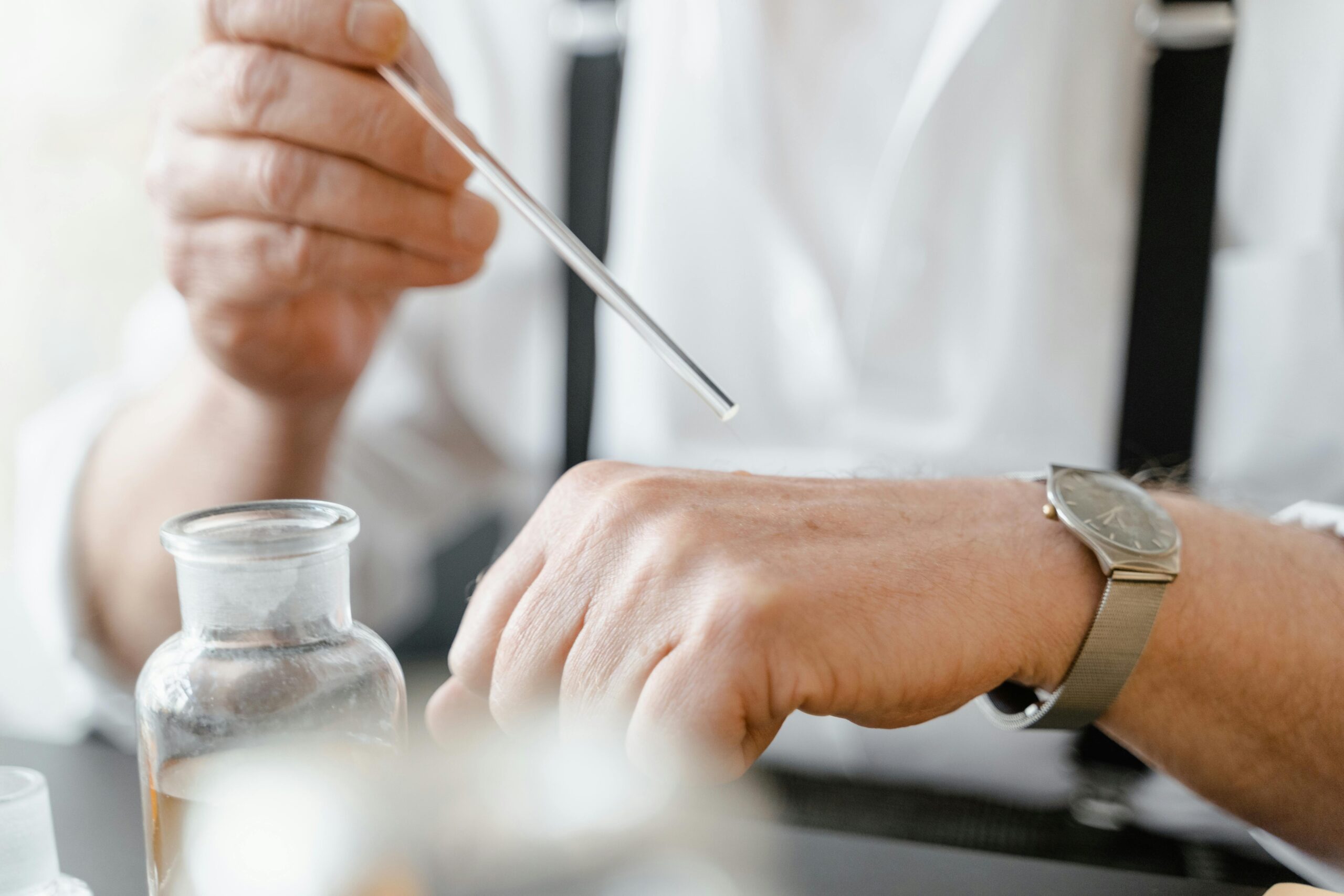 Close-up of a man using a dropper to apply fragrance on his wrist indoors.