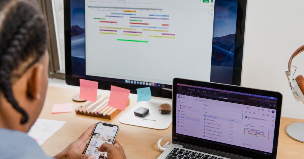 Businessman multitasks with smartphone, laptop, and monitor in office setting.