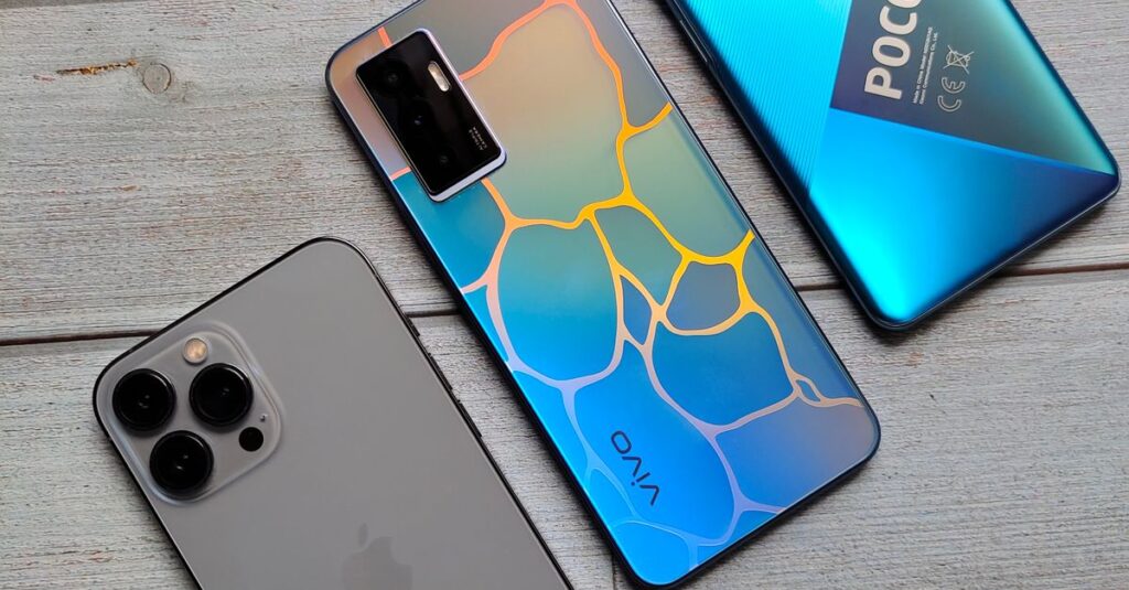 Three different smartphones placed on a wooden surface, highlighting their sleek designs.