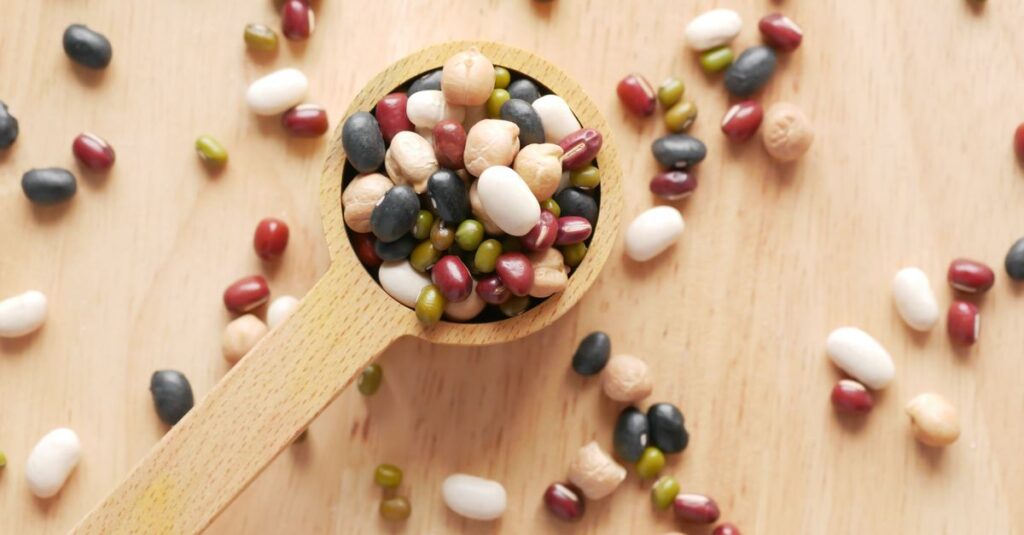 Close-up of assorted beans and legumes on a wooden spoon, showcasing diversity in food ingredients.