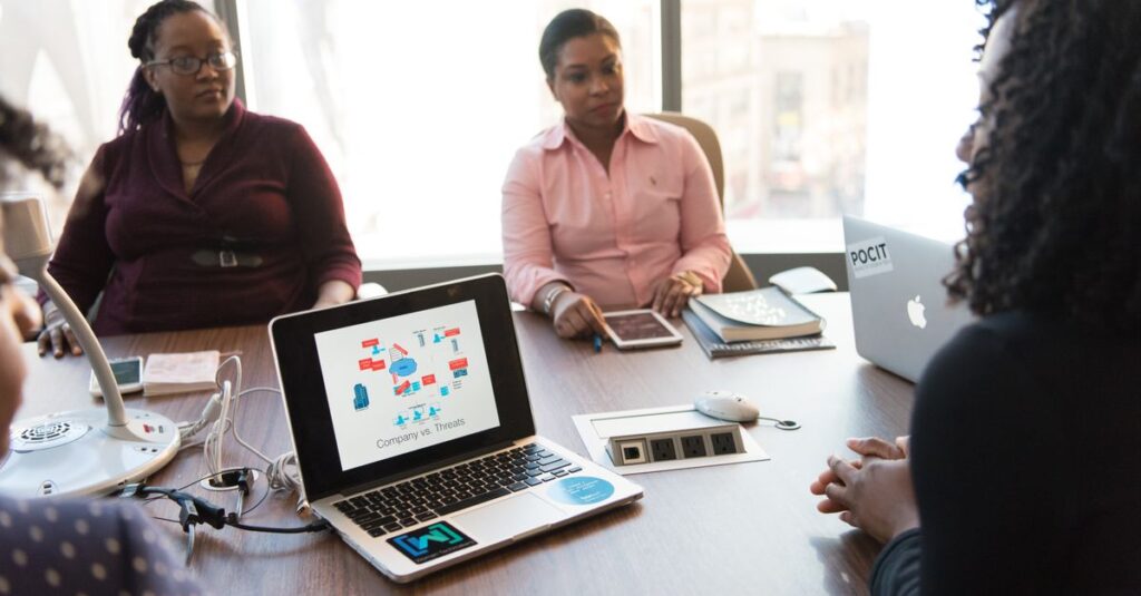 Business meeting with diverse team using laptops and tablets in a modern office setting.