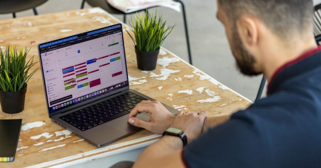 Man working remotely at a desk with a laptop open to a calendar app.