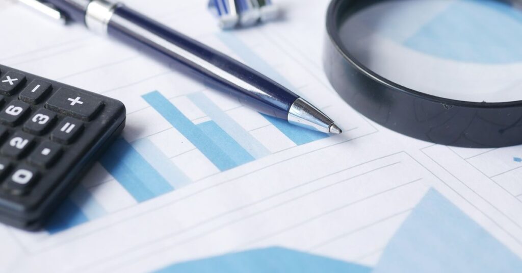 Close-up of calculator, pen, and magnifying glass on financial documents.