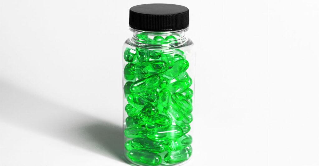 Close-up of transparent bottle filled with green softgel capsules on a white background.