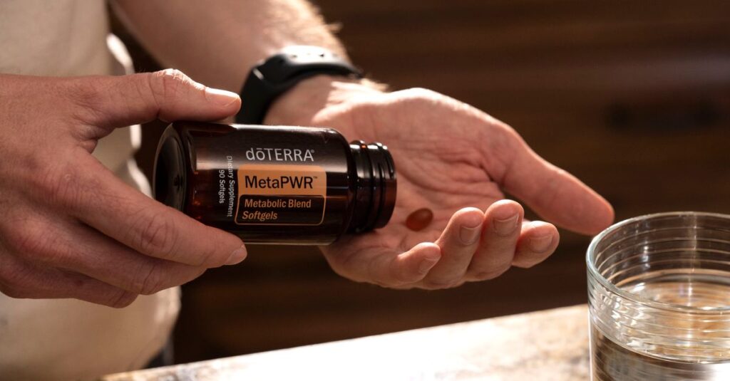 Hand holding MetaPWR metabolic blend softgels next to a glass of water.