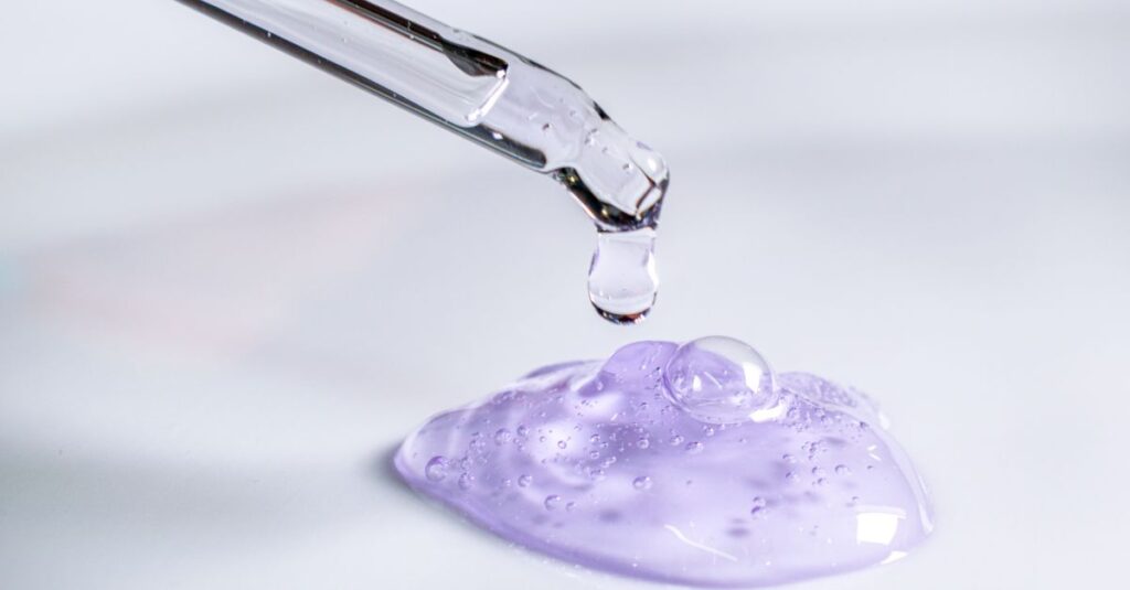 Pipette releasing drop of purple gel, highlighting skincare and laboratory use.