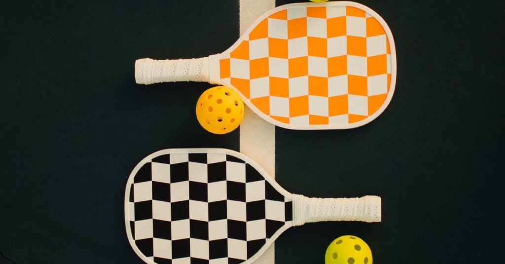 Close-up of four checkered pickleball paddles with matching balls on a court line.
