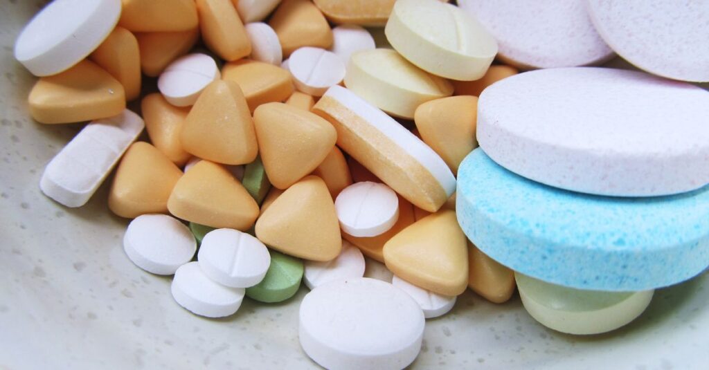 Close-up image of various colorful pills and tablets on a neutral surface.