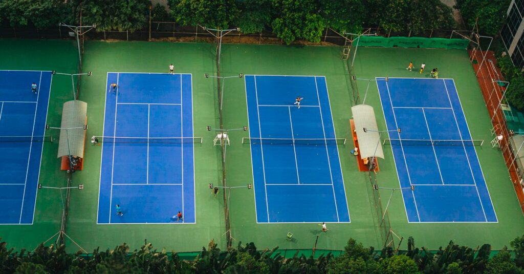 Tennis courts from above showcasing players in action, surrounded by greenery.