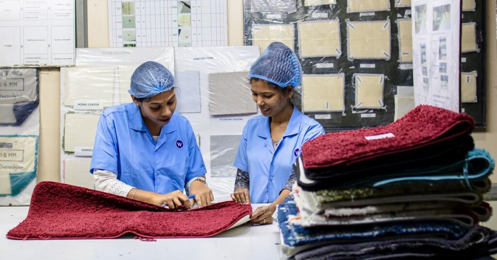 Two women in a textile factory inspecting red fabric samples in an industrial setting.