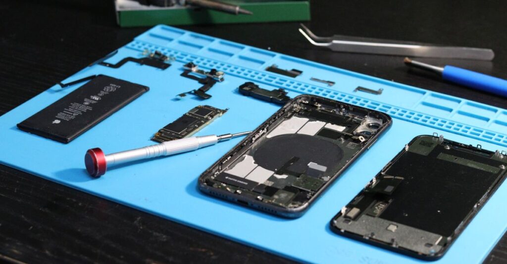Close-up of disassembled smartphone parts on a blue repair mat with tools.