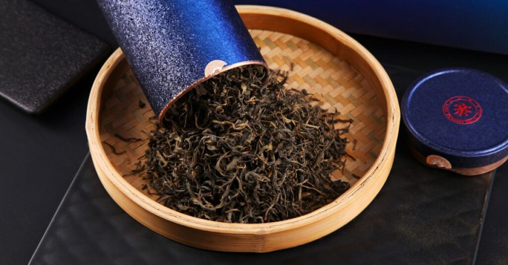Elegant display of loose leaf tea spilling from a blue container into a bamboo plate.