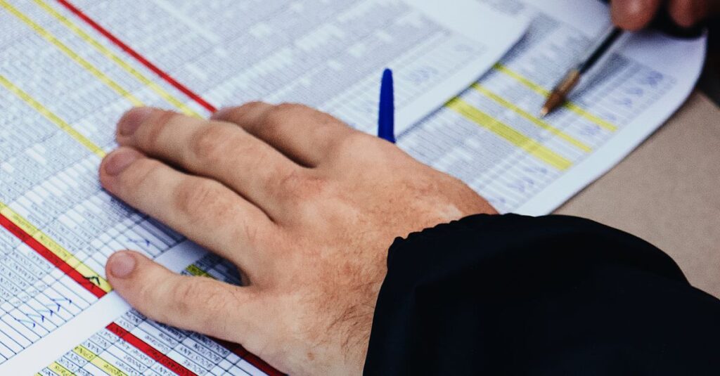 Hands with pen analyzing spreadsheets at a desk, focusing on data and statistics.