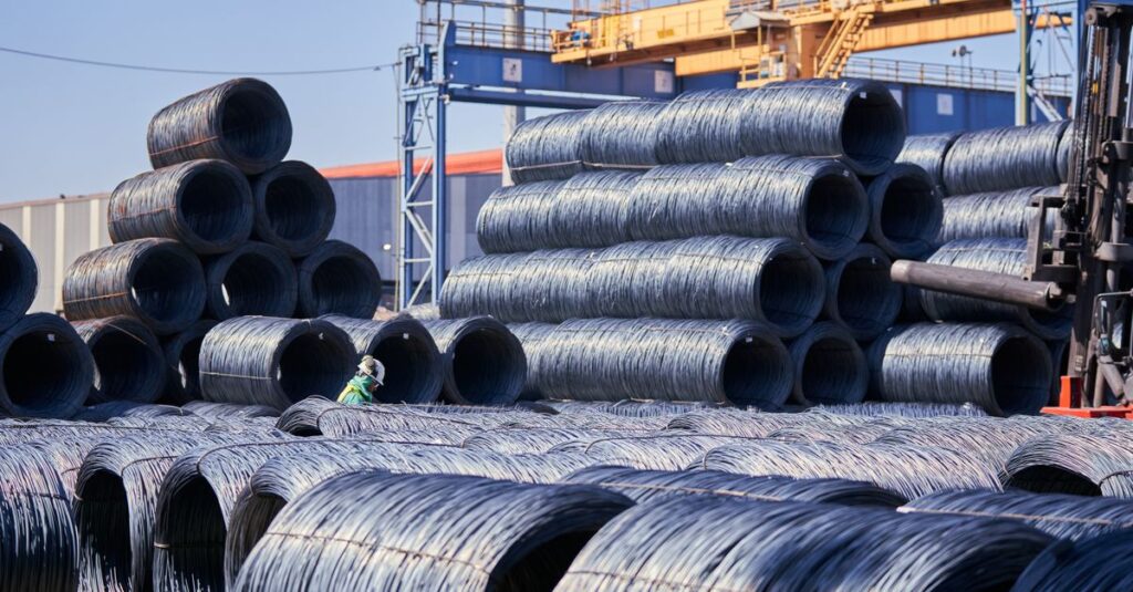 Large stacks of steel wire coils stored outdoors at an industrial site under bright daylight.
