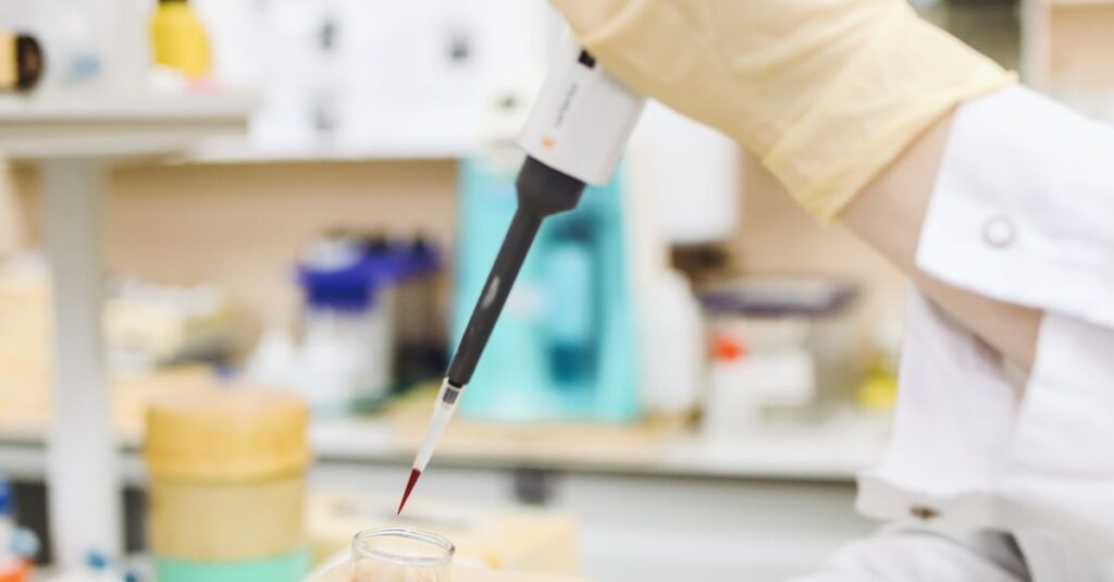 A laboratory technician uses a pipette to transfer red liquid into a beaker in a science lab.