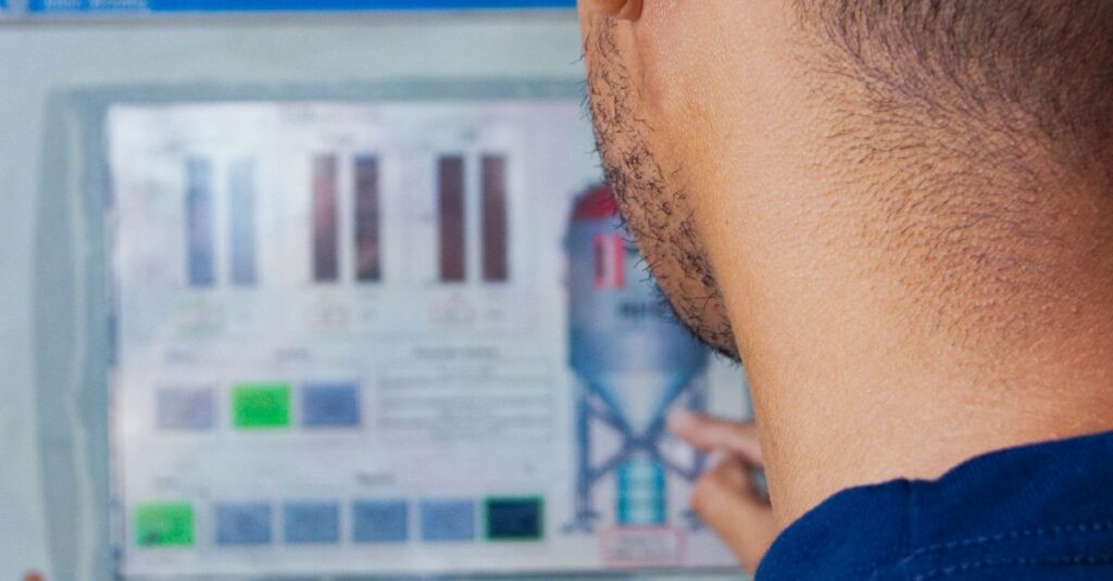 Engineer with hard hat working at an industrial control panel, displaying graphs.