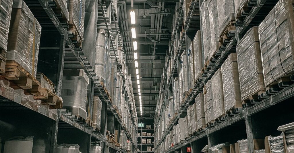 A long aisle in a modern warehouse with high shelving filled with boxes and supplies.
