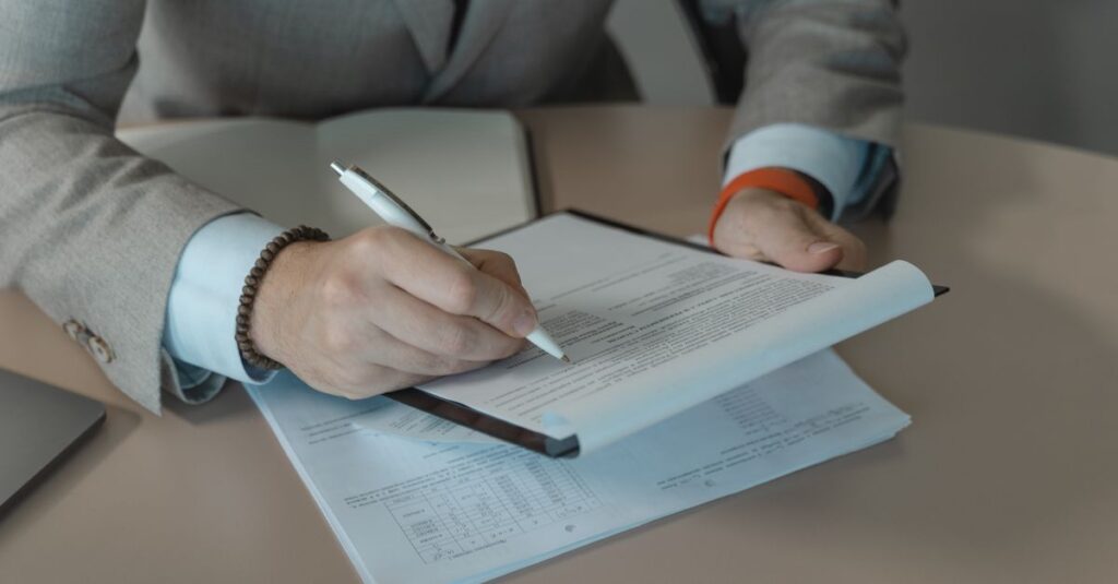 Close-up of business person signing documents at a desk with a pen.