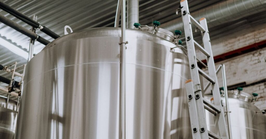 Vertical view of stainless steel fermenter tanks with a metal ladder in a brewery.