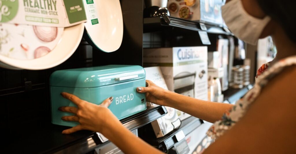 A woman shopping for a turquoise bread bin in a store while wearing a face mask.