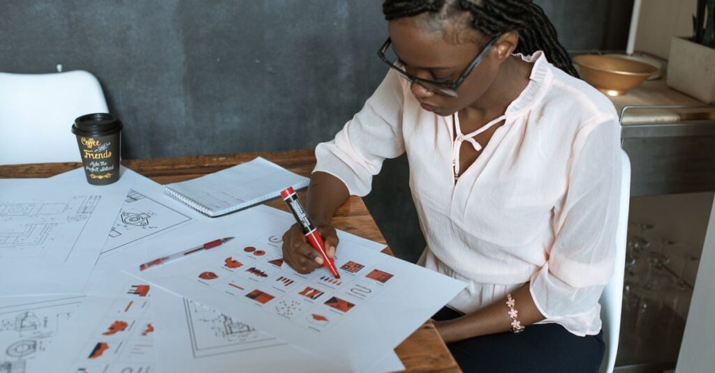 Focused woman drawing architectural plans in office with documents and markers.