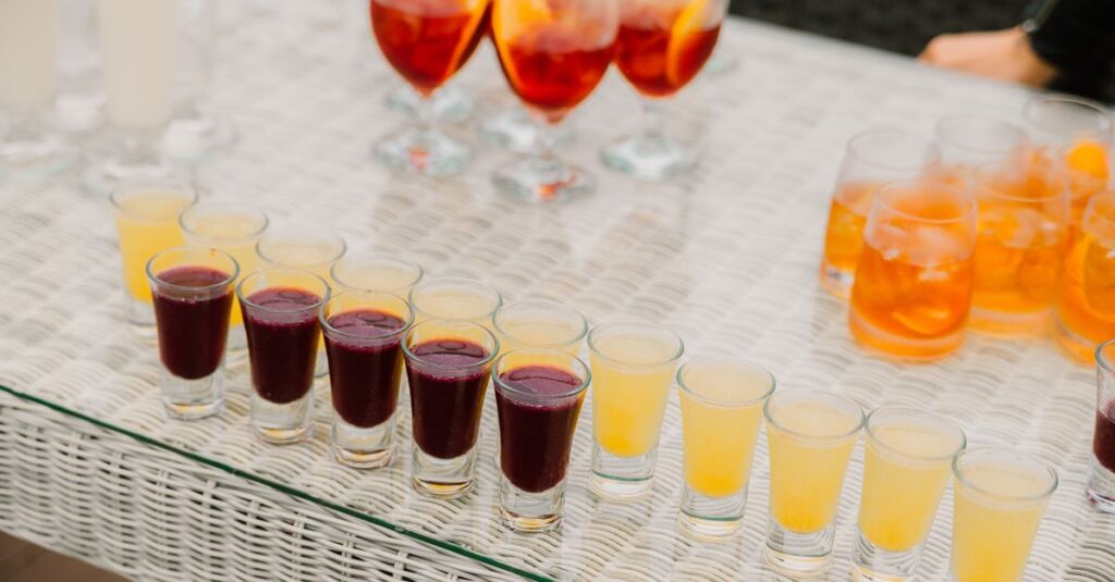 Close-up of colorful drinks in various glasses on a wicker table outdoors.