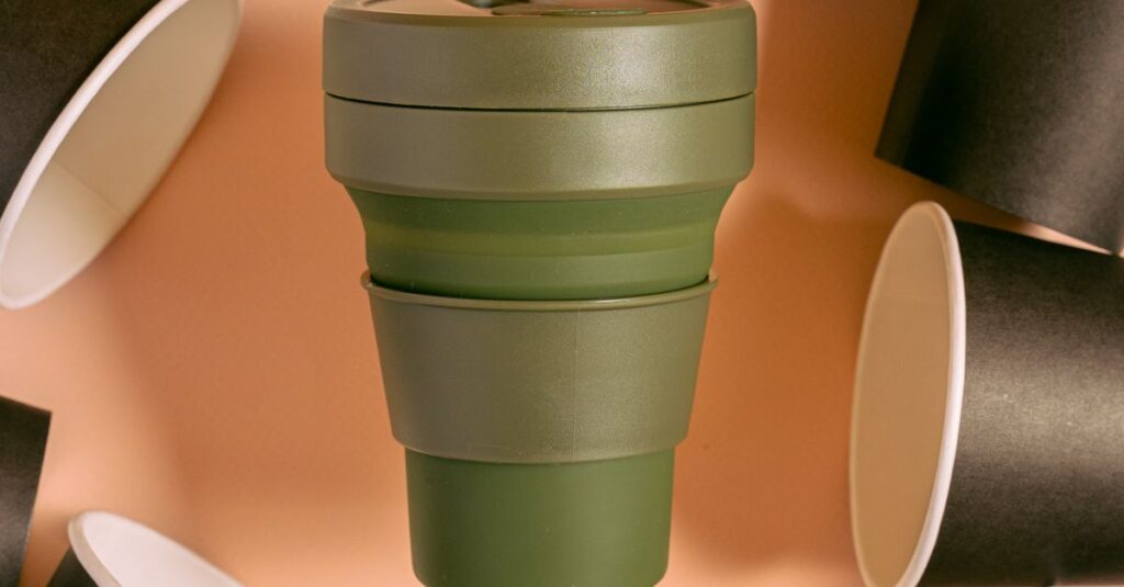 A green collapsible silicone cup among black paper cups, promoting eco-friendly, zero waste living.