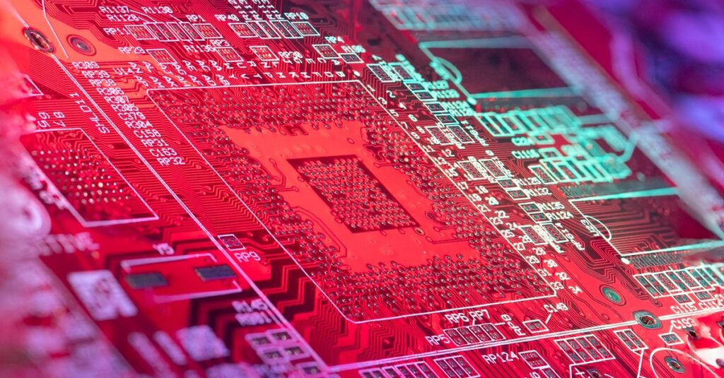 Red printed board of digital device with bright electric circuit with numbers and symbols placed in room on blurred background
