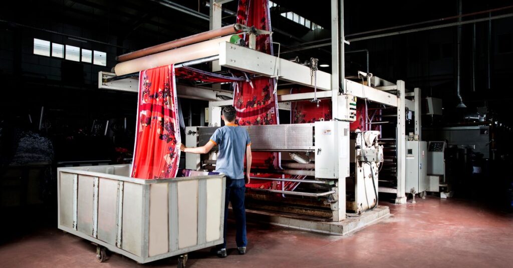 Worker operates machinery in a textile factory, overseeing fabric production.