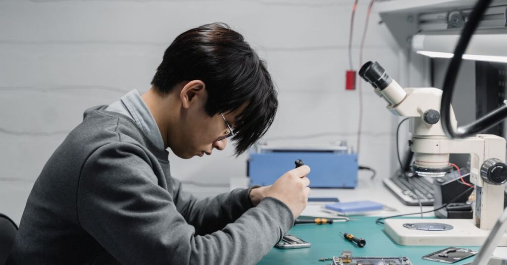 Professional technician repairing mobile devices using a microscope in a lab.