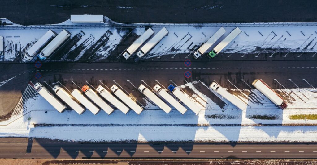 Top-down aerial view of trucks parked in a snowy lot in Poznań, Poland, showcasing winter logistics.