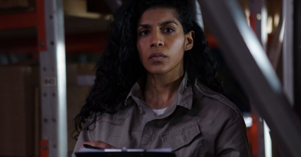 A focused woman holding a clipboard conducting an inventory check in a warehouse aisle.