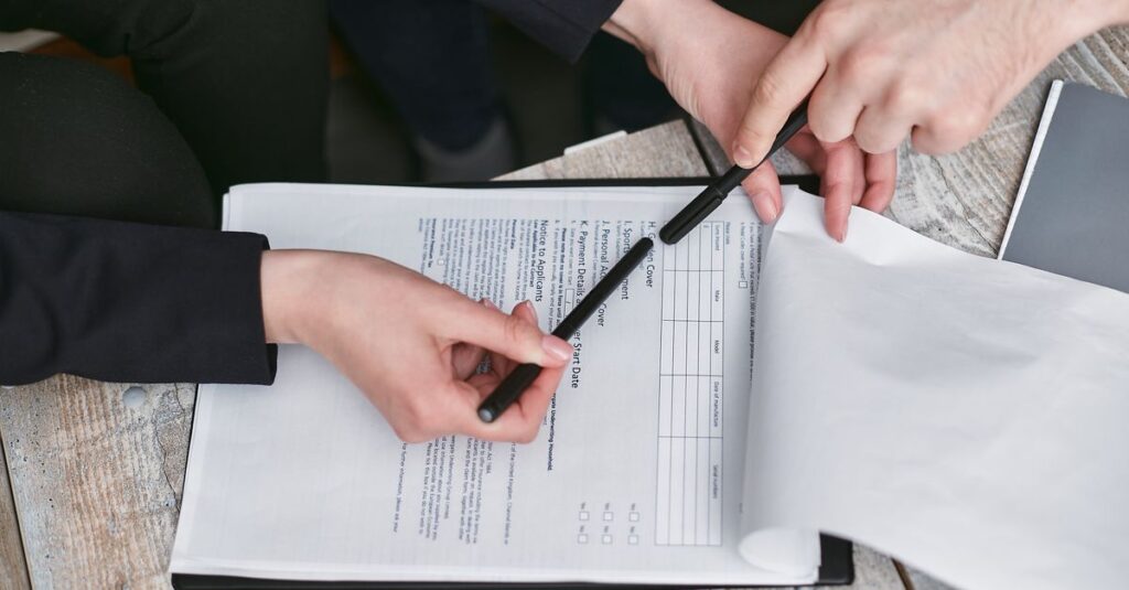 Close-up of business hands finalizing agreement with pen on documents.