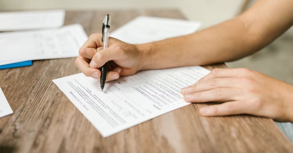 Hand filling out paperwork with a pen, showcasing focus on document completion.