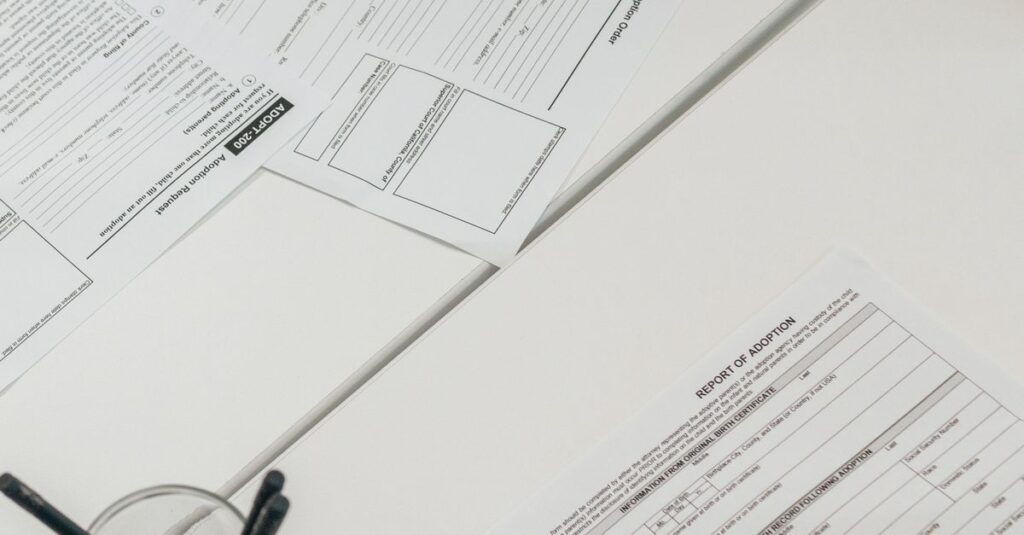 A person holds a pen while examining business documents on a white desk, top view.