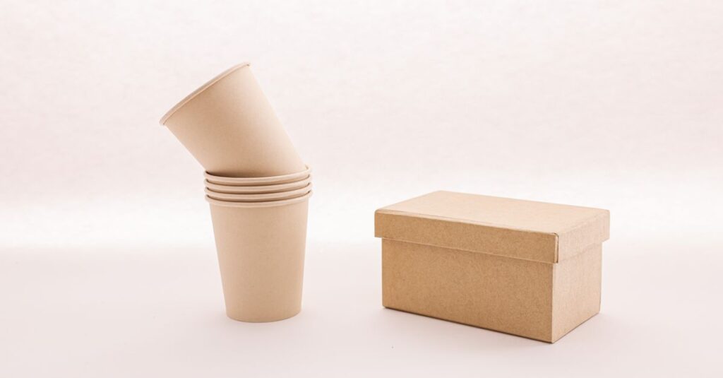 A stack of eco-friendly cardboard cups next to a closed box on a white background.