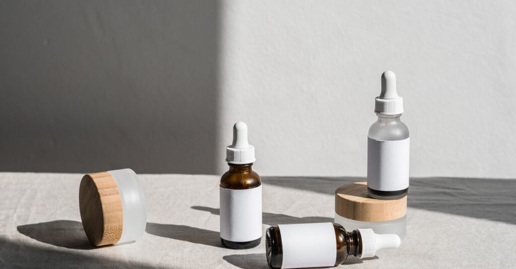 Minimalist composition of beauty bottles with droppers and containers on fabric under natural lighting.