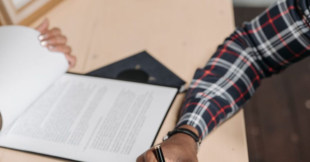 Hands of a person signing official documents on a desk in an office setting.
