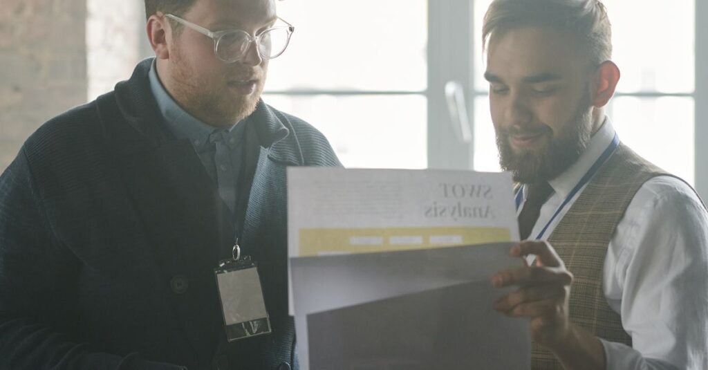 Two businessmen engage in a discussion, reviewing documents indoors.