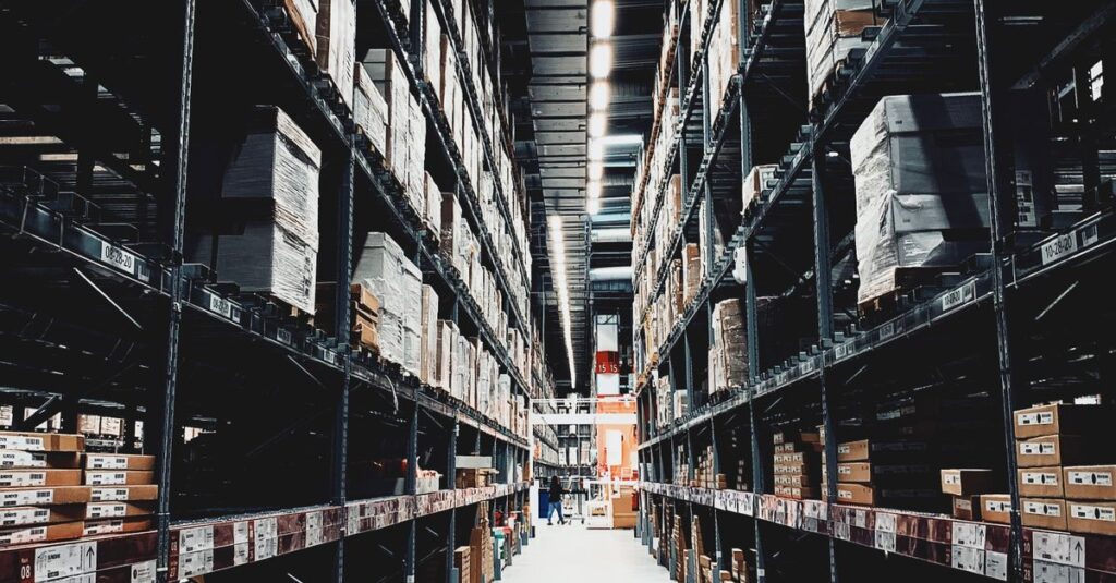 A wide aisle in a large warehouse filled with stacked boxes on high shelves.
