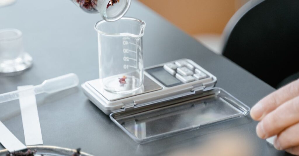 A close-up of hands measuring dried flowers into a beaker on a digital scale, demonstrating laboratory aromatherapy preparation.