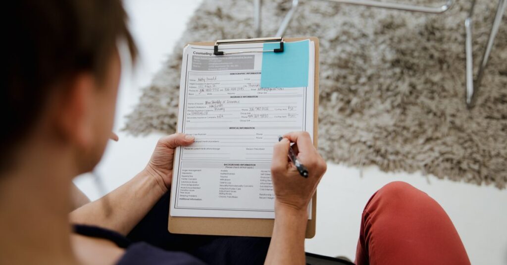 An adult woman writing on a counseling form during a business appointment in an office setting.