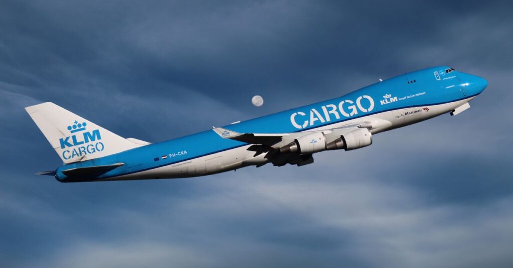 A KLM cargo aircraft flying with the moon in the background, captured during the day.