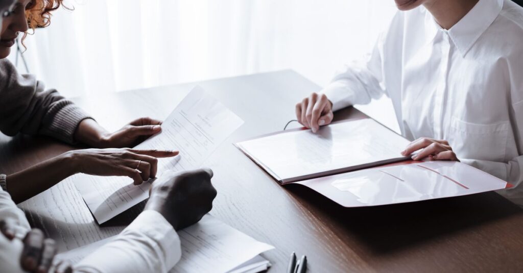 A diverse group of adults reviewing documents during a meeting at an office table.